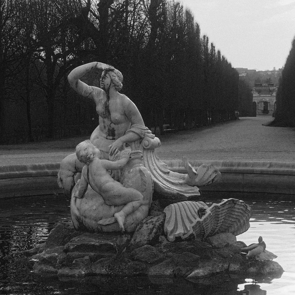 Black-and-white view of a stone fountain sculpture reflected in a garden pond
