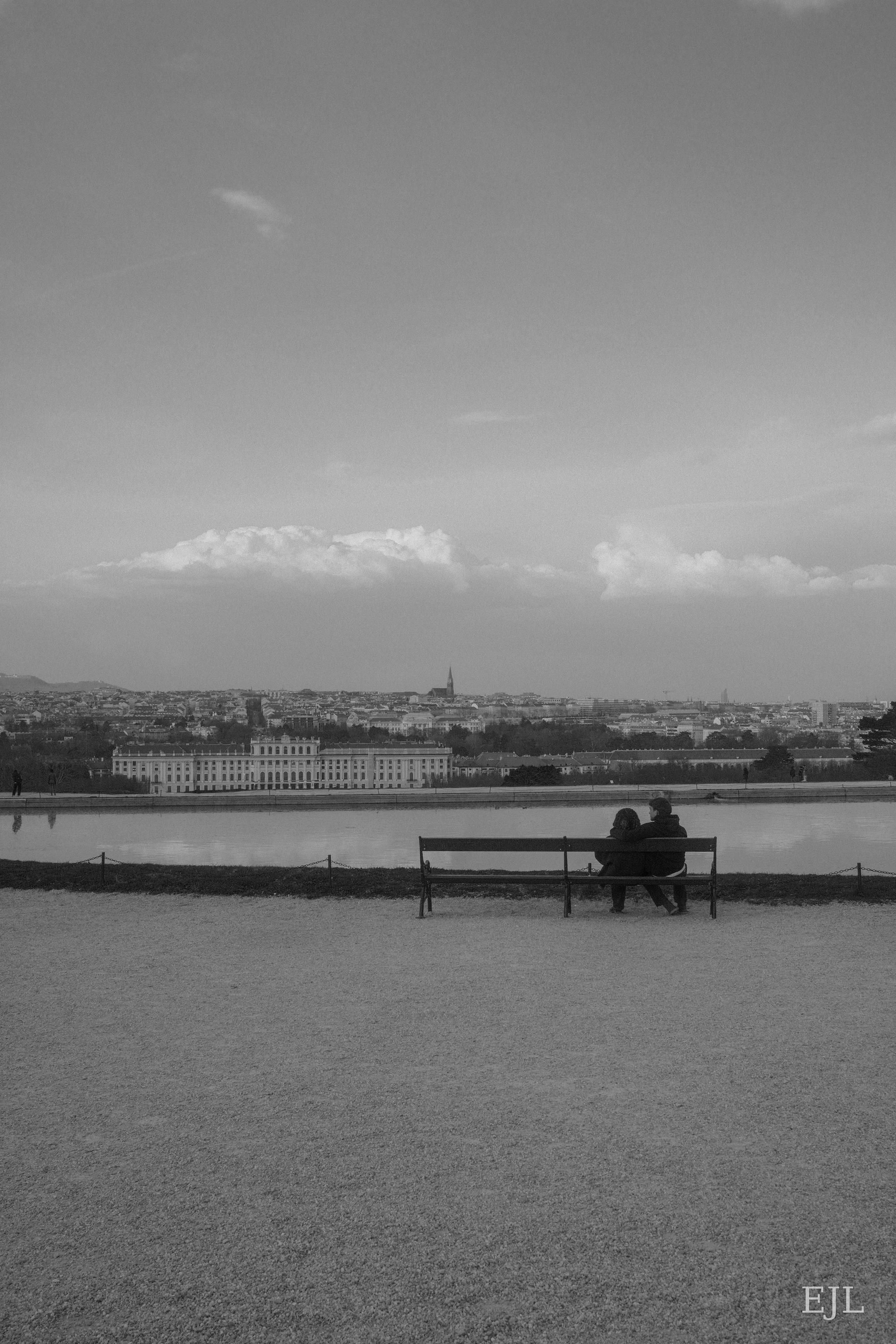 Two people on a bench overlooking a palace and the Vienna skyline in black and white