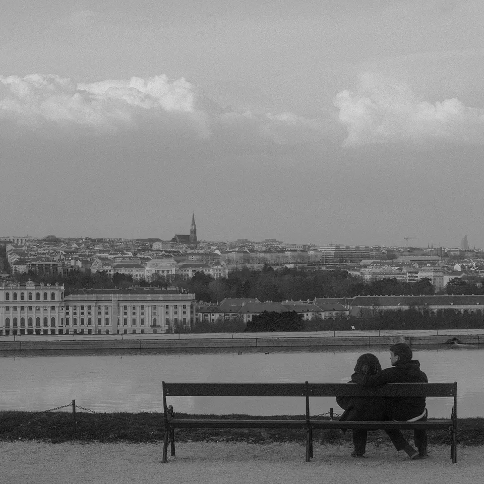 Two people on a bench overlooking a palace and the Vienna skyline in black and white