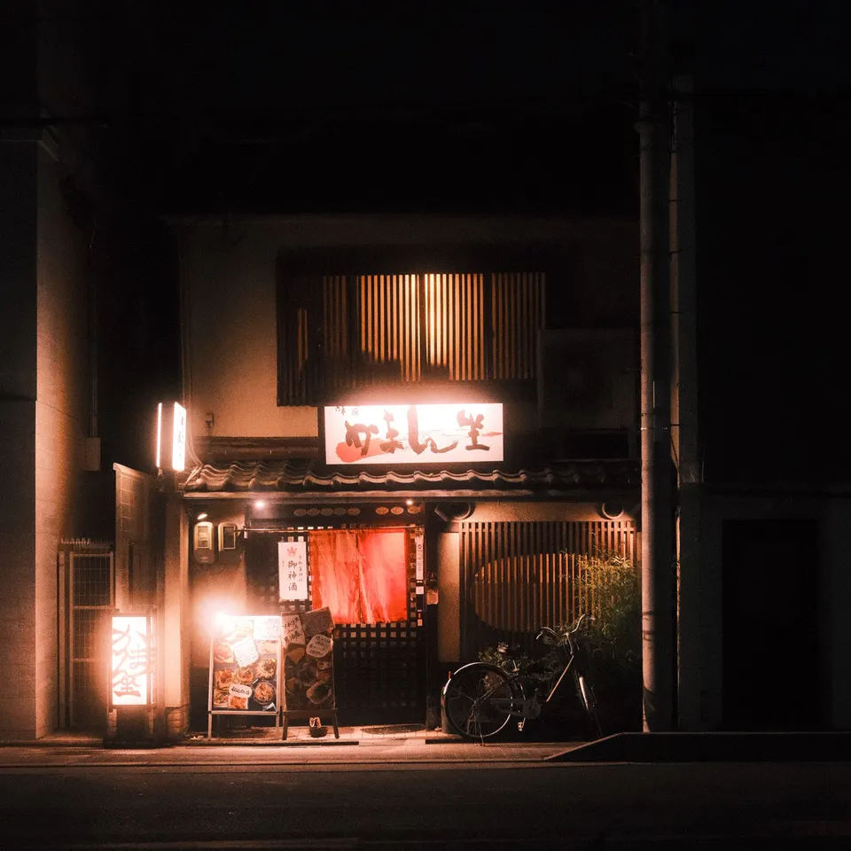 A warmly lit restaurant entrance and a parked bicycle on a dark Kyoto street