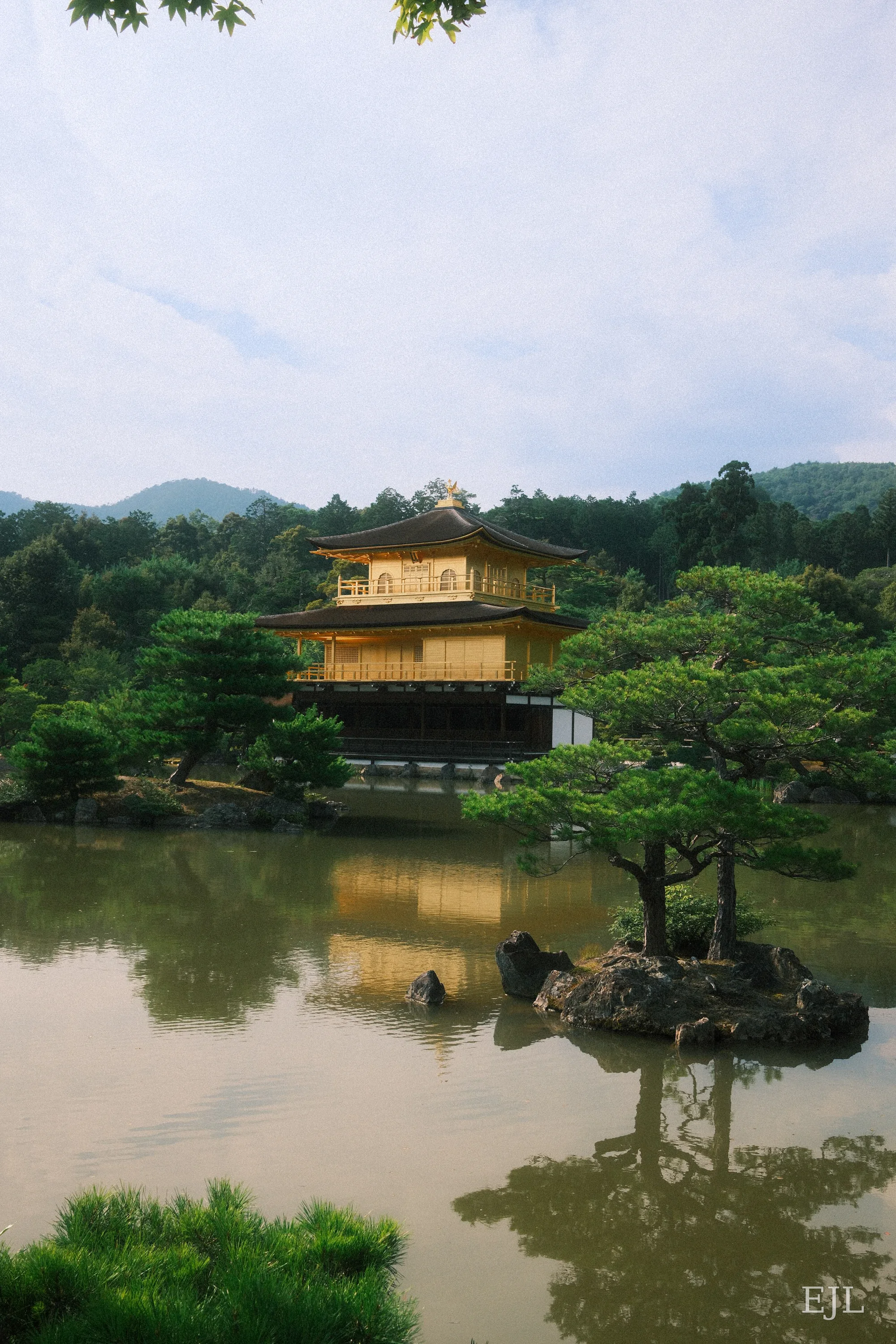 Kinkaku-ji's Golden Pavilion reflected in a pond, framed by pine trees