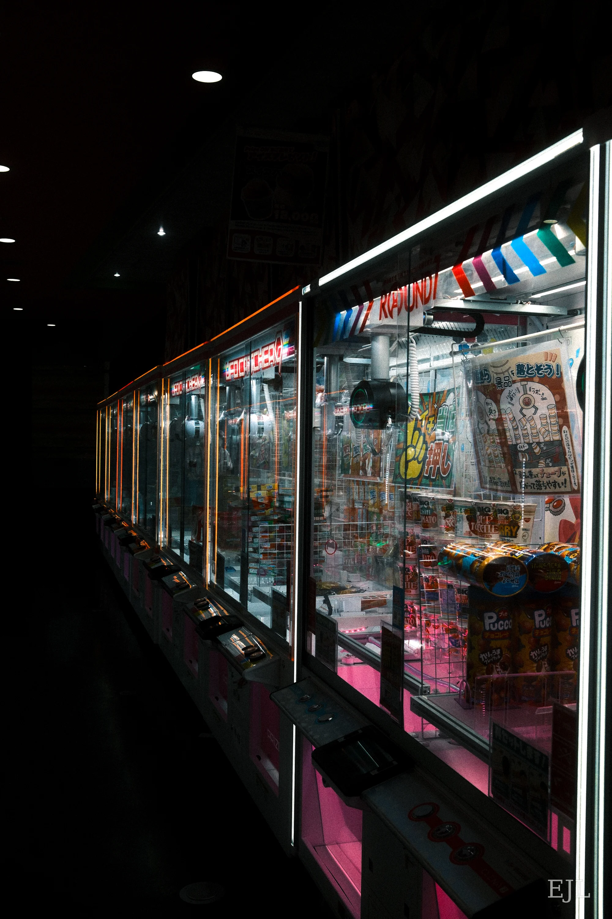 A row of brightly lit claw machines filled with prizes in a dark arcade