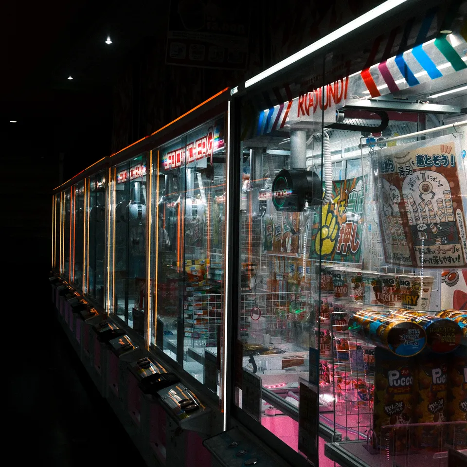 A row of brightly lit claw machines filled with prizes in a dark arcade