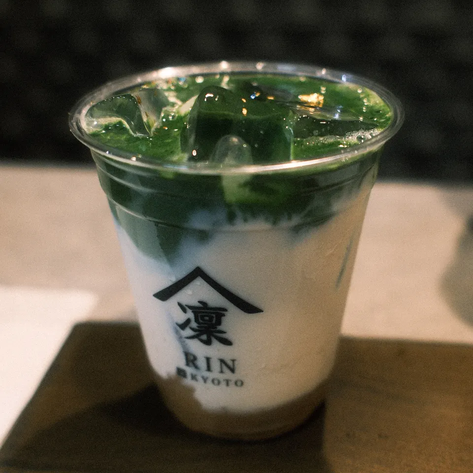 Layers of green matcha and milk in a clear Rin Kyoto cup on a wooden tray