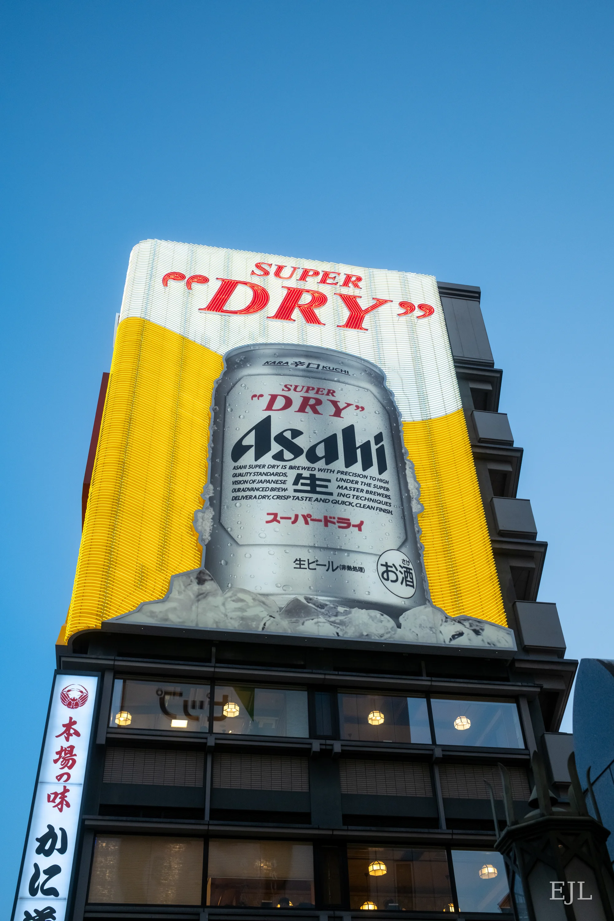 A large yellow Asahi Super Dry billboard above an Osaka building against a blue sky