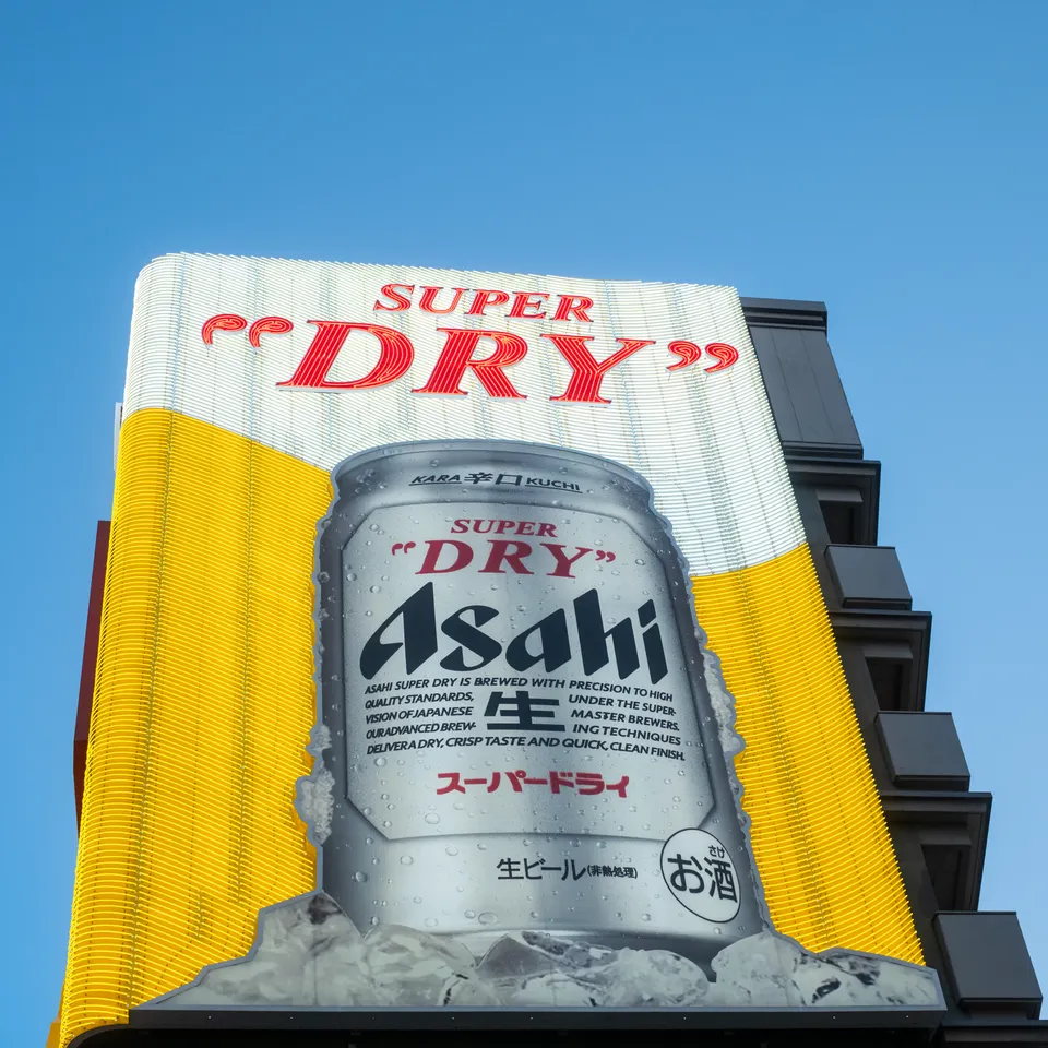 A large yellow Asahi Super Dry billboard above an Osaka building against a blue sky