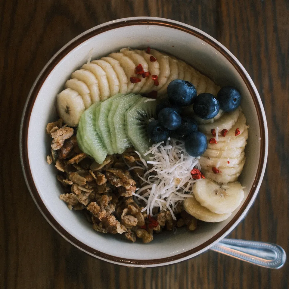 A granola bowl topped with sliced banana, kiwi and blueberries on a wooden table