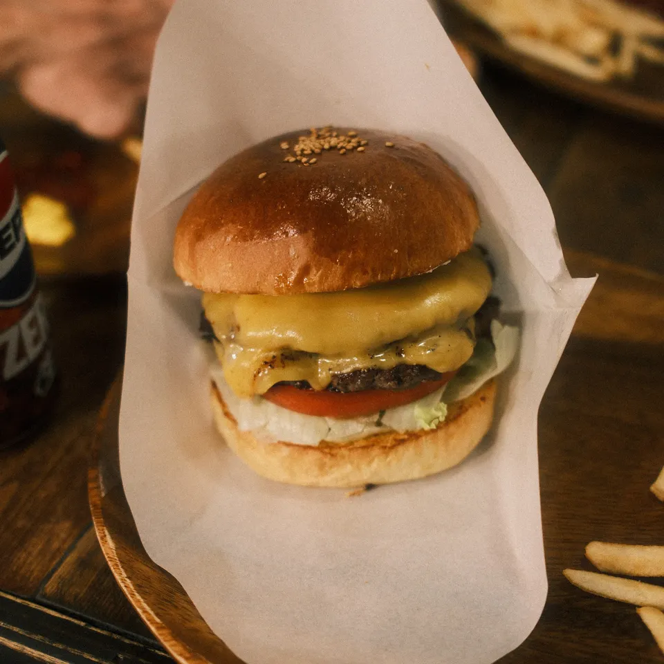 A cheeseburger with a glossy bun, lettuce and tomato in a paper-lined basket