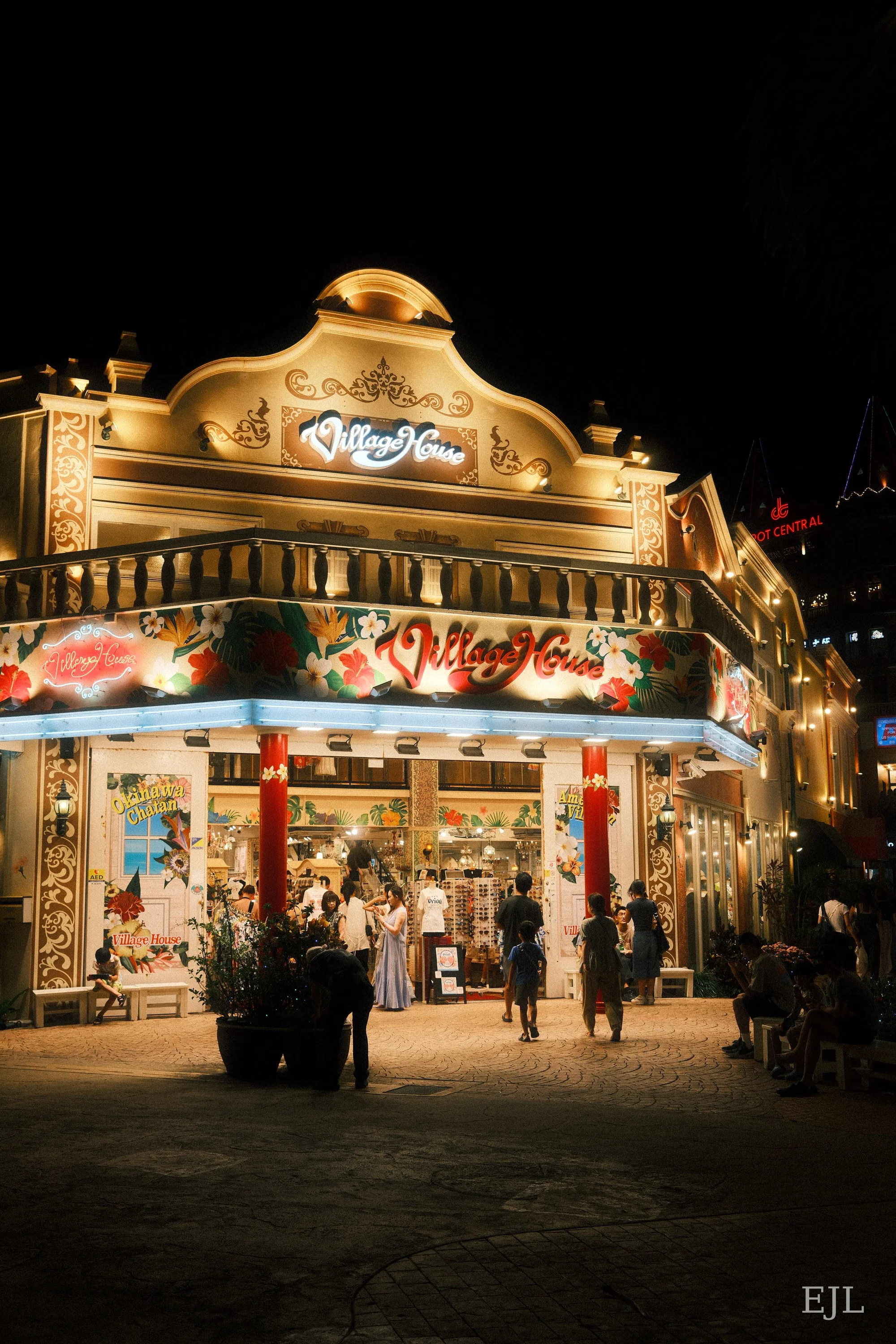 The illuminated Village House storefront with shoppers outside at night