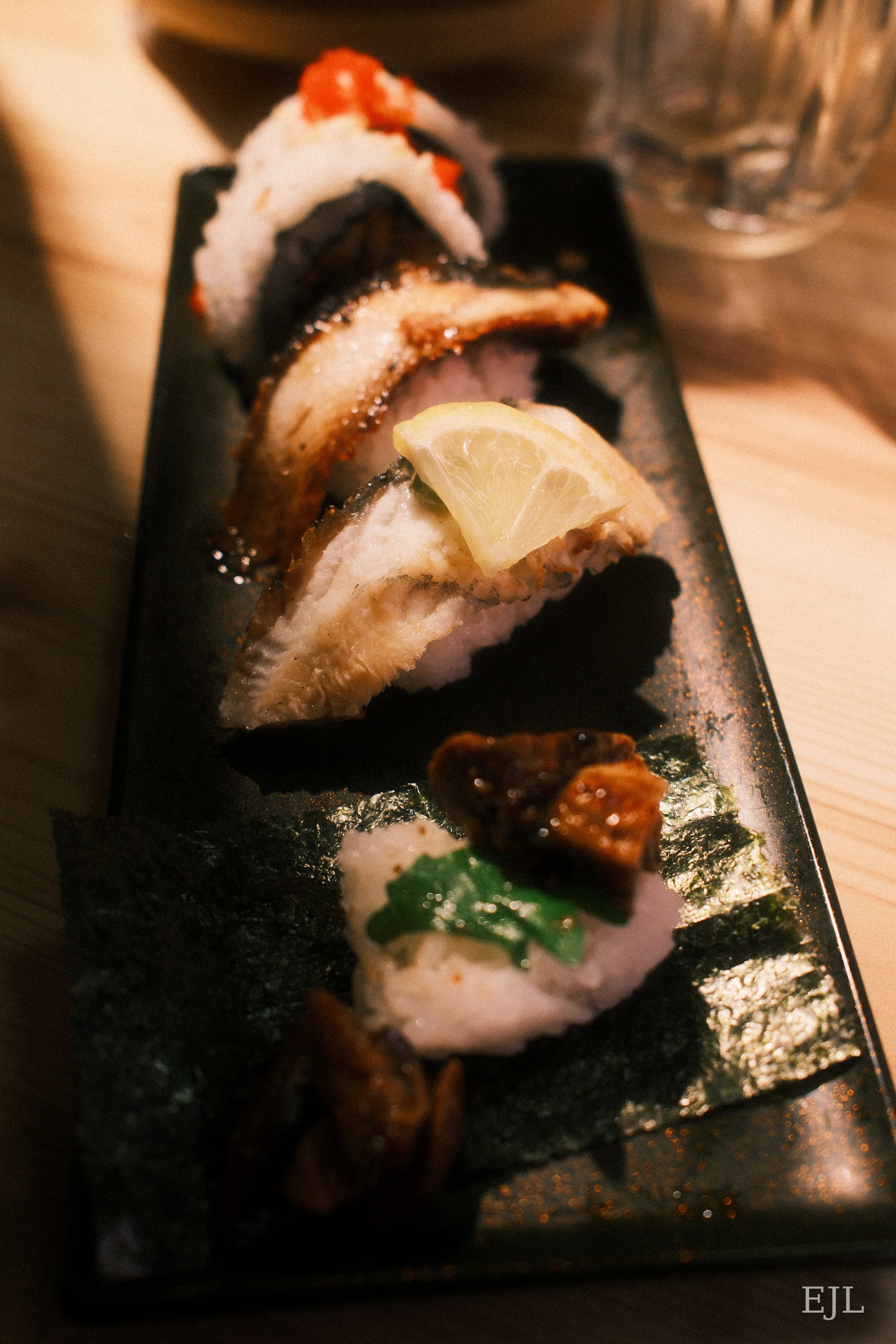 Sushi with grilled eel, a lemon slice and garnishes on a long black plate