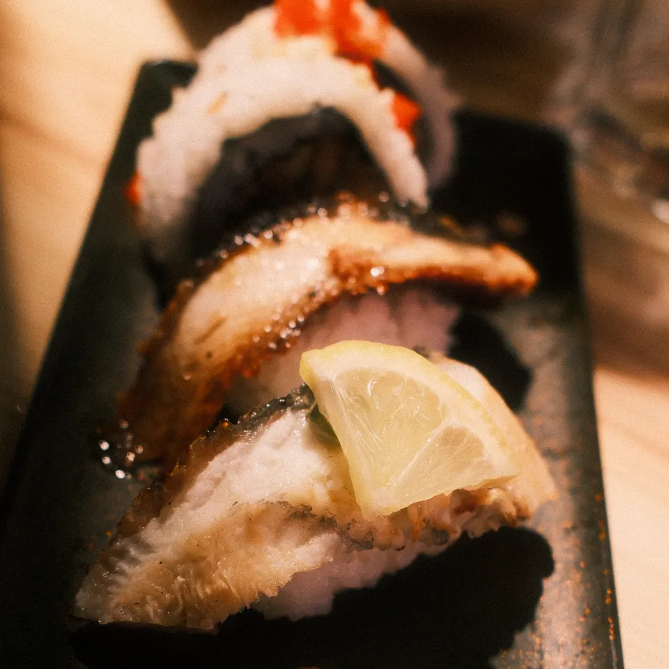 Sushi with grilled eel, a lemon slice and garnishes on a long black plate