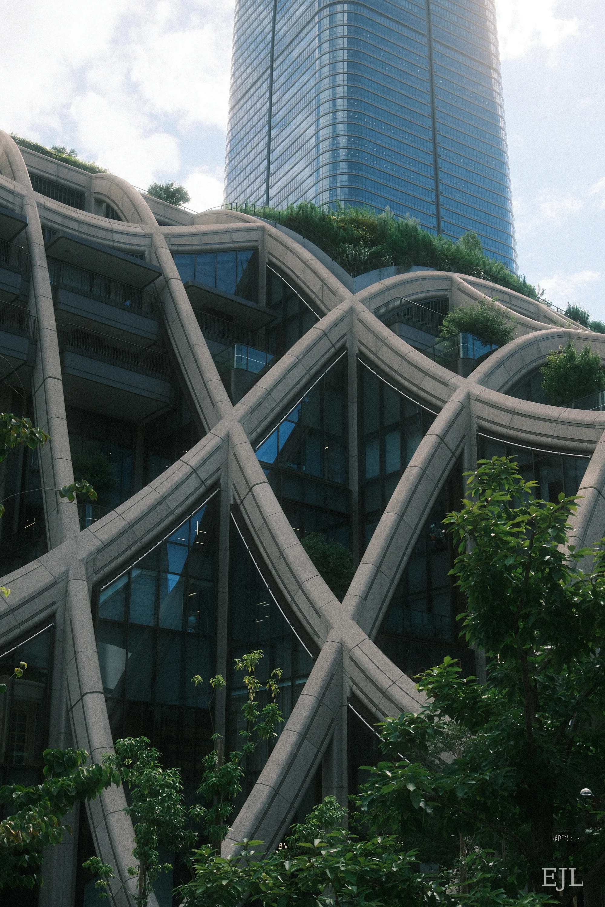 Curving concrete latticework and planted terraces at Azabudai Hills, with a tower behind