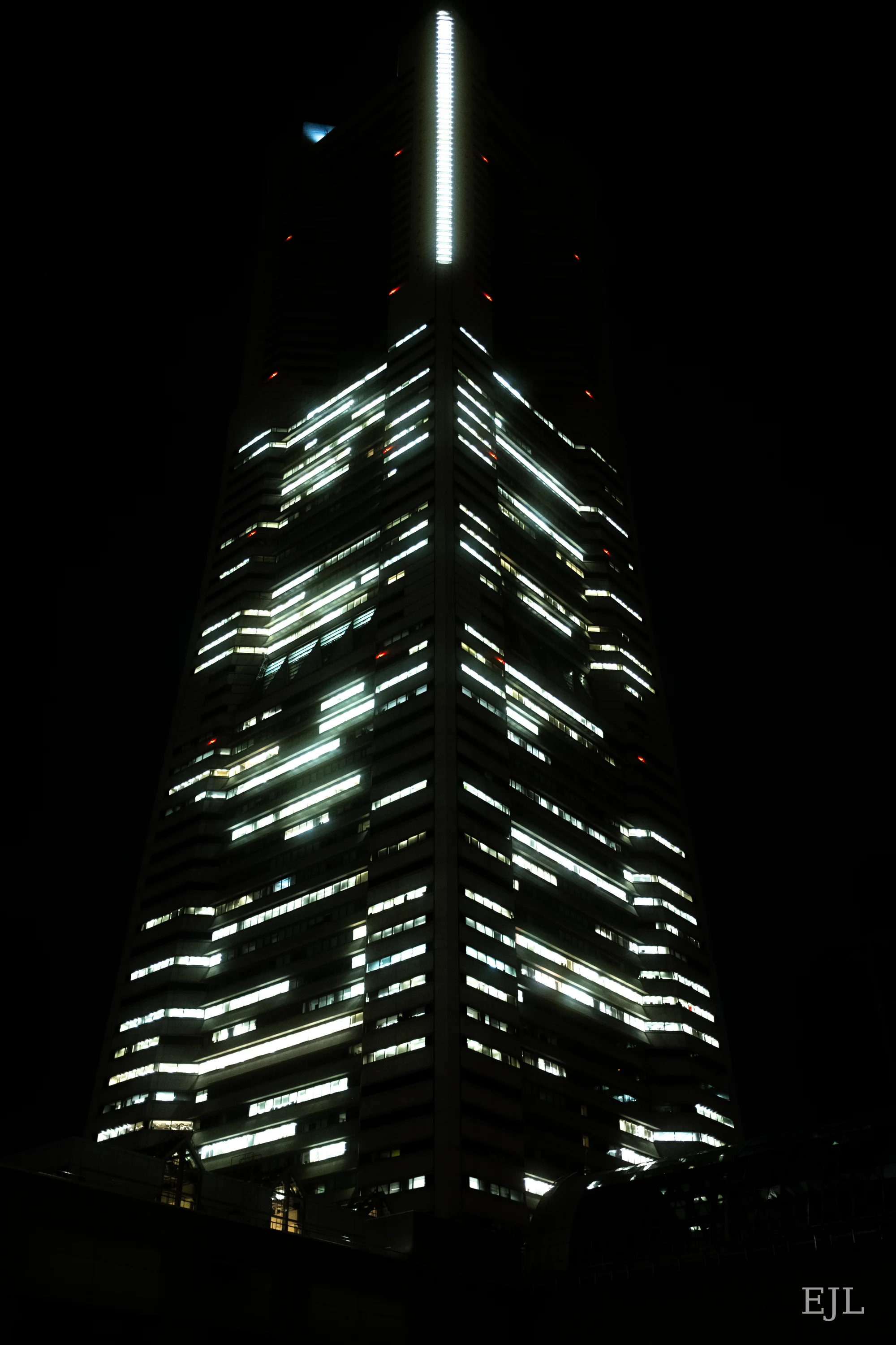 Bright horizontal windows and a vertical light strip on a skyscraper against the night sky