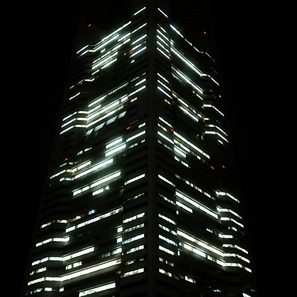 Bright horizontal windows and a vertical light strip on a skyscraper against the night sky